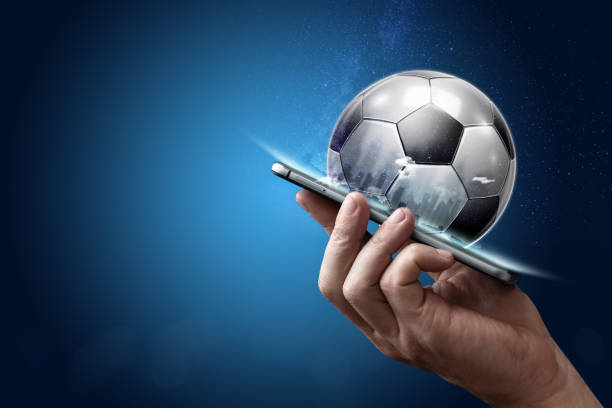 Smartphone in hand with a 3D soccer ball on a blue background. Bets, sports betting, bookmaker. Mixed media stock photo
