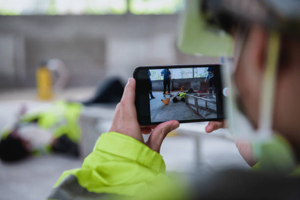 Smartphone shooting on accidents and Unconscious of worker in workplace at construction site area while having the Medical assistance first aid team with equipment. stock photo