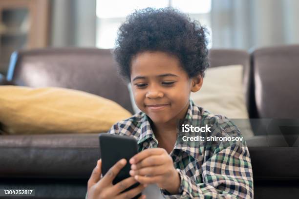 Smiling adorable schoolboy in casual shirt looking at screen of smartphone