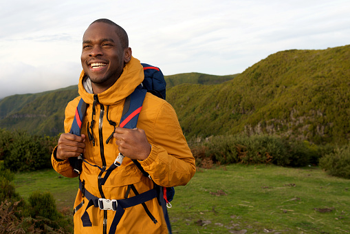 Portrait of smiling african american hiker walking with backpack in nature