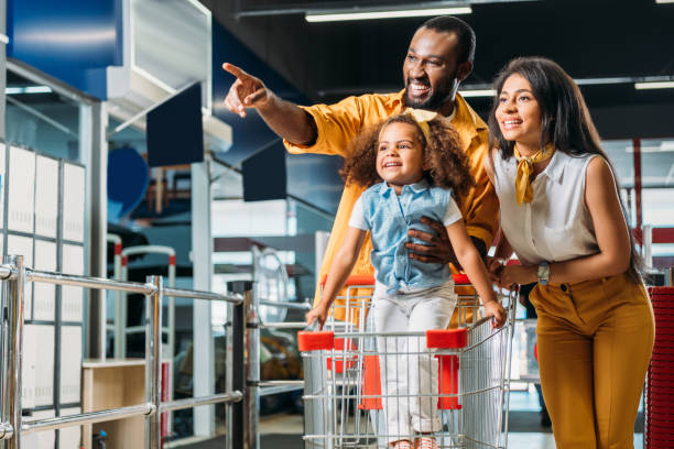 smiling african american man pointing by finger to little daughter and wife in supermarket smiling african american man pointing by finger to little daughter and wife in supermarket cart photos stock pictures, royalty-free photos & images
