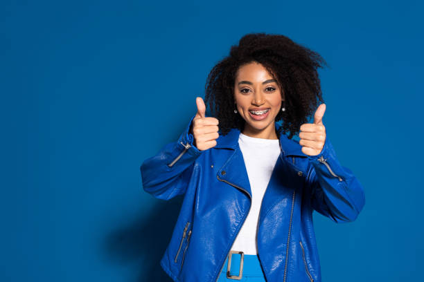 smiling african american woman showing thumbs up on blue background smiling african american woman showing thumbs up on blue background dental braces stock pictures, royalty-free photos & images