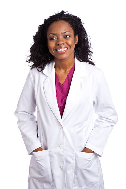 Smiling African ethnicity female wearing lapcoat hands in pockets "Beautiful happy mid adult female wearing lap coat, hands in pockets, isolated on white background" lab coat stock pictures, royalty-free photos & images