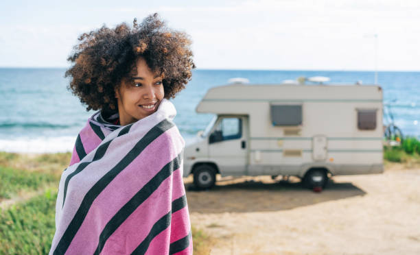 Smiling afro women which is wrapped with a beach towel enjoying her summer vacation with camper stock photo