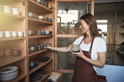 Smiling artisan organizing pottery on shelves in her creative gallary