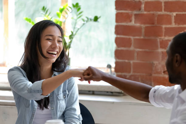 lachende aziatische zakenvrouw met afro-amerikaanse collega vuisten bump - high five stockfoto's en -beelden