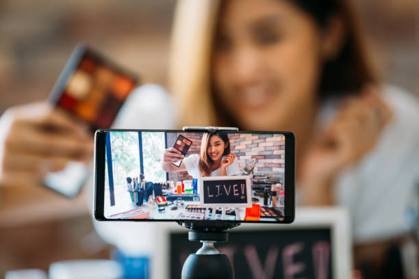 smiling asian woman showing eyeshadows on display of smartphone - smartphone filming imagens e fotografias de stock