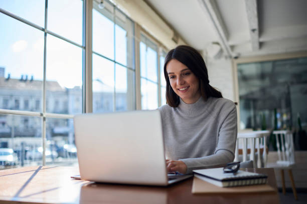 Smiling attractive female freelancer doing remote job using laptop computer stock photo