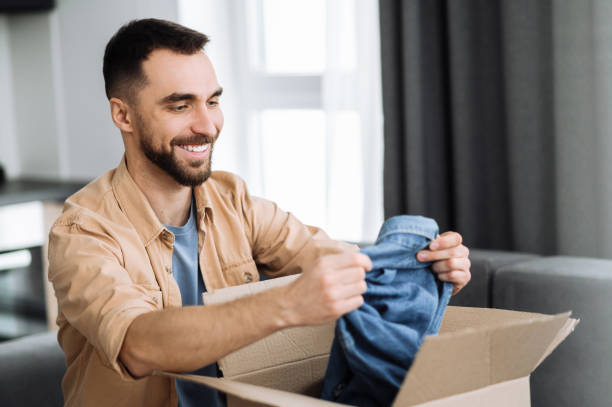 Smiling attractive man unpacked his parcel, happy about getting a long expected order. Caucasian modern guy shopping in internet stores, buying new clothes online, online shopping concept stock photo