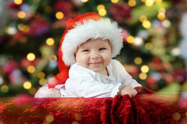 A smiling baby in a Santa hat in front of Christmas lights stock photo