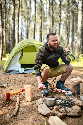 Smiling Bearded Male Chopping Wood And Making Skewered Meat In Forest Camp