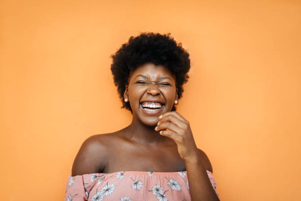 Smiling black young woman at orange wall stock photo