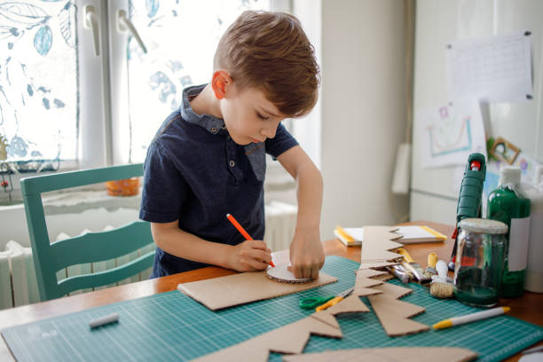 улыбающийся мальчик делает картонный костюм динозавра - прикладное искусство стоковые фото и изображения