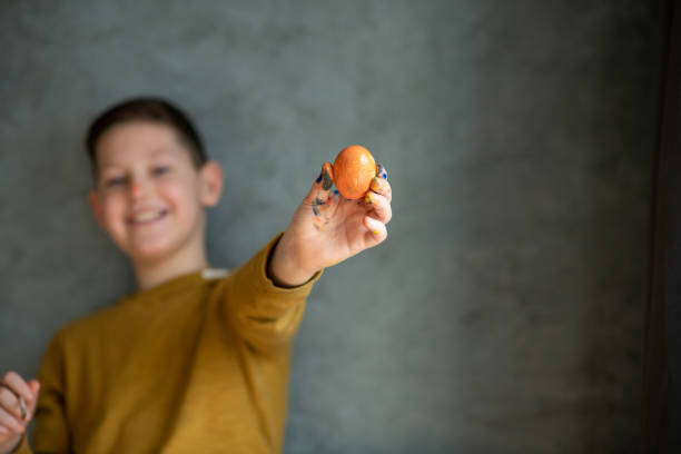 Smiling boy shows orange Easter egg. Copy space. Selective focus.  easter sunday stock pictures, royalty-free photos & images