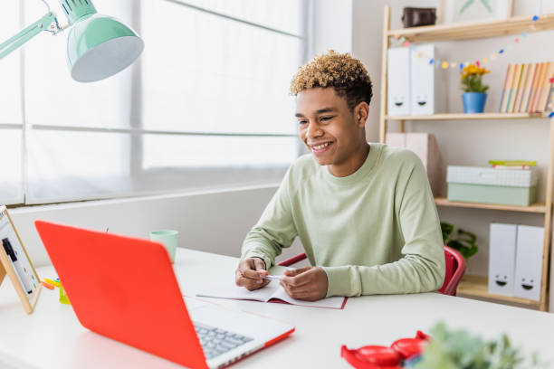 Smiling boy studying online from home having a video conference on laptop stock photo
