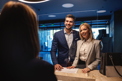 A smiling business couple with positive vibes and energy standing at the hotel reception and checking in. Free weekend, relationship, business trip, recharging a battery