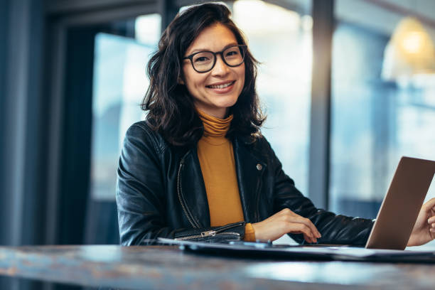 Smiling business woman in casuals at office Portrait of attractive business woman sitting at her desk with laptop computer in office. Smiling business woman in casuals at office. east asian ethnicity stock pictures, royalty-free photos & images