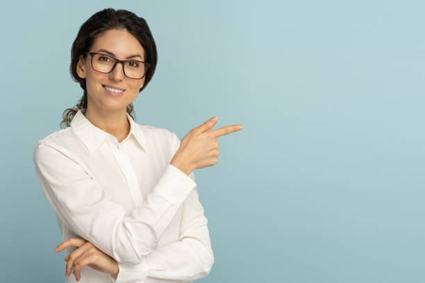 Smiling business woman wear white blouse and glasses pointing with finger, showing at copy space Smiling business woman wear white blouse and glasses pointing with finger, showing blank copy space for advertising, offering, product, promotion, sale, isolated on studio blue background human finger stock pictures, royalty-free photos & images
