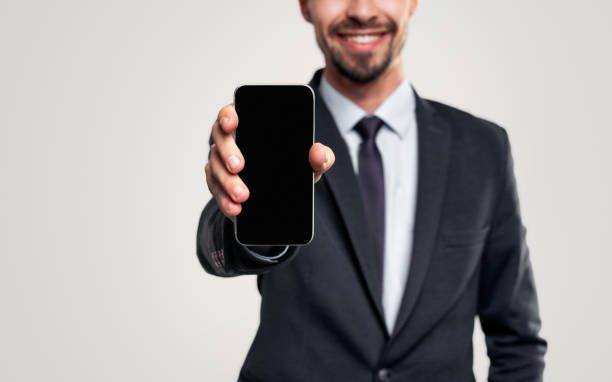 Smiling businessman in suit showing smartphone stock photo