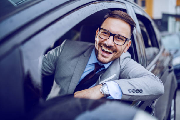 Smiling businessman looking trough window while driving his expensive car. Business trip concept.  man driving suit stock pictures, royalty-free photos & images