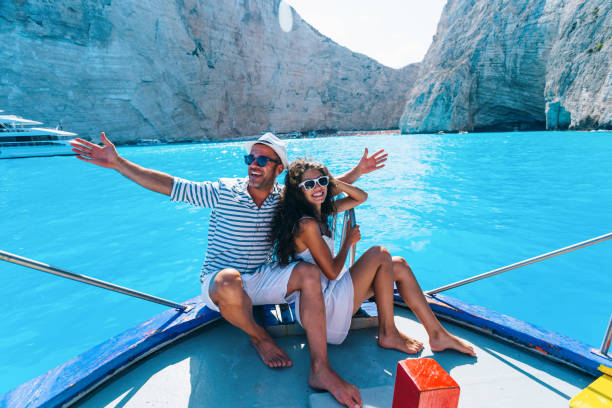 smiling caucasian couple on the board of a sailing boat in the water near navagio beach, greece - navagio beach stockfoto's en -beelden