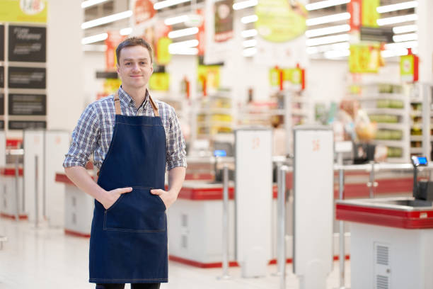 Smiling caucasian seller stands holding hands in pockets with superstore on background stock photo
