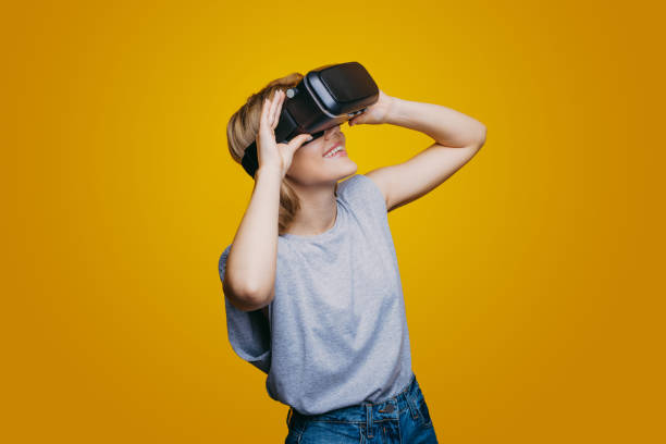 Smiling caucasian woman wearing virtual headset. Using VR glasses. Yellow wall background. Future technology. Smart device. stock photo