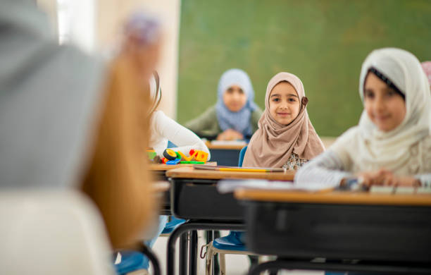 Smiling children in class A cute little muslim girl smiles as she sits in class learning. She is listening to her teacher talk from the front of the room. cute arab girls stock pictures, royalty-free photos & images