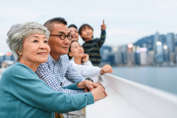 Smiling Chinese Senior Couple Enjoying Hong Kong Views Relaxed senior Chinese woman and husband enjoying Hong Kong views with extended family at Ocean Terminal Deck atop Harbour City Shopping Centre. hong kong photos stock pictures, royalty-free photos & images
