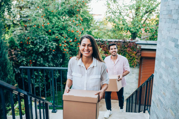 Smiling couple carrying boxes into their new house. Portrait of happy young couple moving to new house with cardboard boxes. Couple move into their new home. Smiling couple carrying boxes into new home on moving day. Young family entering in their new house. first time home buyer stock pictures, royalty-free photos & images