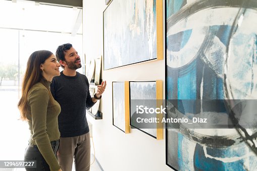 istock Smiling couple is looking at the paintings that are for sale at an art exhibition 1294597227