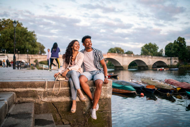 Smiling Couple Sitting on Embankment in Richmond Upon Thames Relaxed couple sitting on the Richmond Riverside embankment in the late afternoon with a weekend of leisure ahead of them. city break stock pictures, royalty-free photos & images