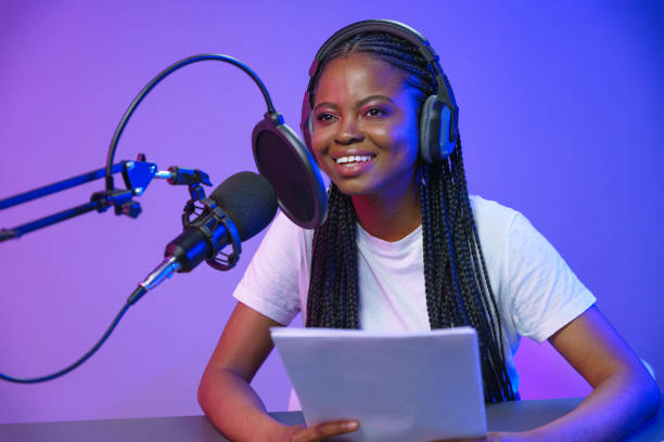 Smiling dark skinned podcaster with braids in a white t-shirt during he record with the script in her hands stock photo
