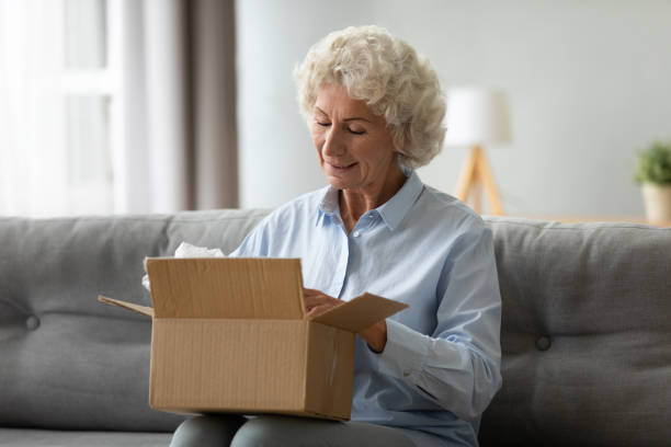 pelanggan wanita lanjut usia yang tersenyum menerima paket pengiriman pos di rumah - pembukaan kegiatan potret stok, foto, & gambar bebas royalti