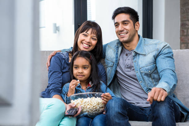 Smiling family eating popcorn while watching tv Smiling family eating popcorn while watching tv in living room asian kids watching tv stock pictures, royalty-free photos & images