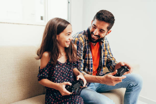 Smiling father and daughter playing video game at home Smiling father and daughter playing video game at home pardo brazilian stock pictures, royalty-free photos & images