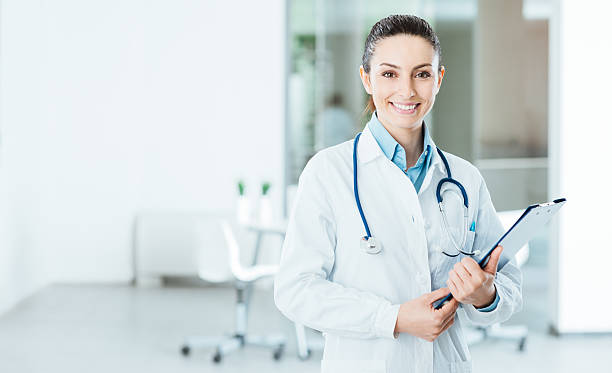 Smiling female doctor holding medical records Smiling female doctor with lab coat in her office holding a clipboard with medical records, she is looking at camera female doctor stock pictures, royalty-free photos & images