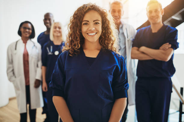 Smiling female doctor standing with medical colleagues in a hospital Smiling young female doctor standing in a hospital corridor with a diverse group of medical staff standing behind her medical clinic stock pictures, royalty-free photos & images