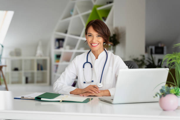 Smiling female doctor using laptop while working at doctor's office stock photo