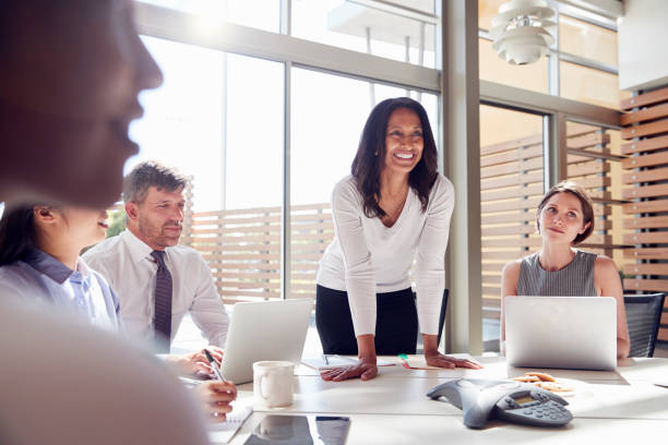 lachende vrouwelijke manager luisteren naar collega's tijdens een vergadering - windows laptop table stockfoto's en -beelden