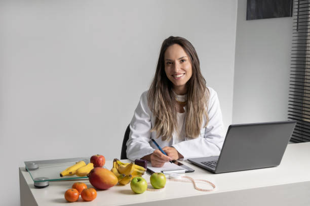 Smiling female nutritionist in her office, writing diet plan showing healthy vegetables and fruits. Healthcare and diet concept. Lifestyle. stock photo