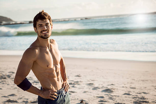 smiling fit man relaxing after workout strong fit man smiling and taking a break after hard workout,beautiful weather,sunny day,in the background waves splashing on the beach male bodybuilders stock pictures, royalty-free photos & images