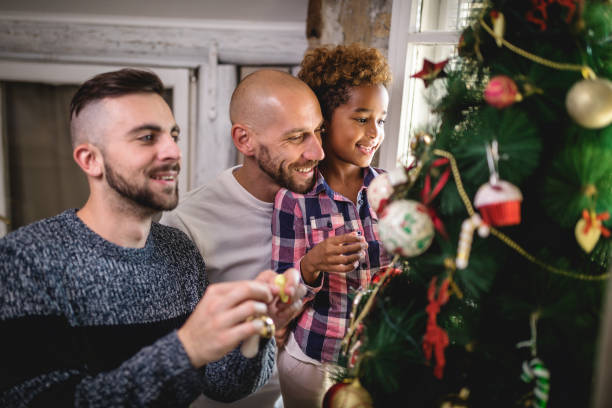 Smiling gay family and their adopted daughter decorating a tree stock photo