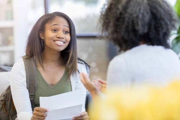 Smiling girl holds college acceptance letter Happy African American teenage girl smiles while holding a college acceptance letter. She is meeting with a guidance counselor. school counselor stock pictures, royalty-free photos & images