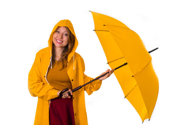 Smiling girl in yellow raincoat stands under umbrella isolated on white background stock photo