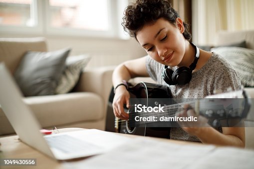 istock Smiling girl playing a guitar at home 1049430556