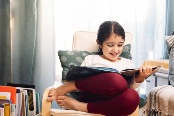 smiling girl reading sitting at home - child reading imagens e fotografias de stock