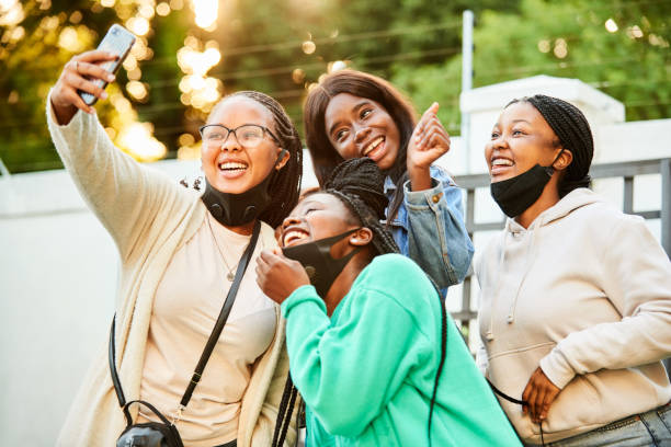 Smiling group of teenage girls taking masks off to take selfies together outside stock photo