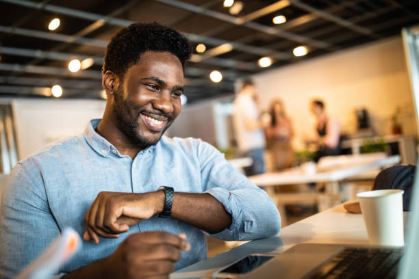 Smiling Haitian man in  modern office Handsome Haitian male entrepreneur  sitting  in modern office space, looking at laptop and laughing beautiful haitian women stock pictures, royalty-free photos & images