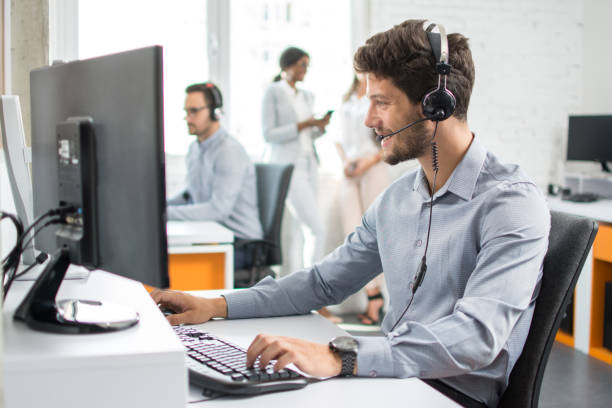 Smiling handsome customer support operator agent with hands-free device working in call center stock photo